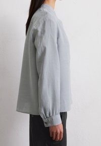 Ljusgrå linneskjorta med avslappnad passform, lång ärm och knäppta manschetter. Har en mandarinkrage och en minimalistisk design.