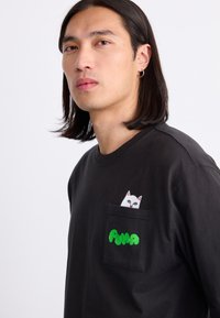 Black T-shirt made of cotton, featuring a front pocket with a white cat design and green "PUMA" text in a playful, rounded font.