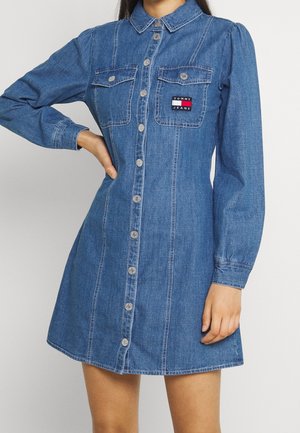 Vestido camisa de mezclilla con cuello con solapa, mangas largas, dos bolsillos en el pecho y cierre de botones en la parte delantera. Tejido azul desgastado con costuras en contraste.