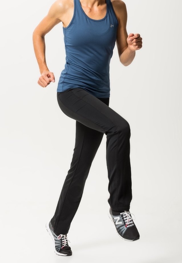 Osoba v modrém tílku a černých kalhotách běhá nebo se pohybuje na místě, má na sobě černobílé tenisky na bílém pozadí.