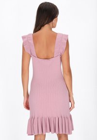 Geribbelde roze jurk met een diepe V-rug, rimpelige schouderbanden en een flared zoom. De stof heeft een gladde textuur.