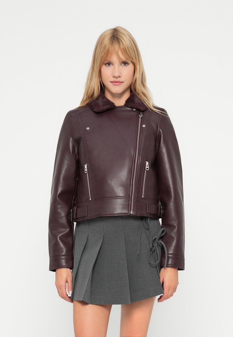 Bordeaux leren motorjack met een faux fur kraag, ritszakken en een cropped ontwerp, gecombineerd met een grijze plooirok.