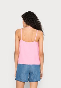 Top sem mangas de cor rosa claro com alças finas e um ajuste descontraído, combinado com calções de ganga. Textura suave e design minimalista.