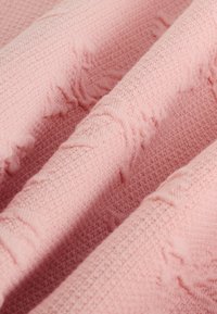 Tessuto rosa strutturato con motivo a cialda, caratterizzato da bordi morbidi e leggermente sfrangiati, drappeggiato in pieghe sovrapposte.