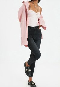 High-waisted black skinny jeans, white fitted top with embellishments, and a light pink oversized shirt. Black shoes with buckle detail.