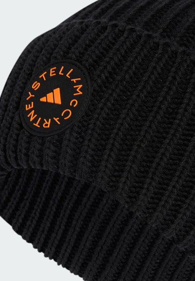 Melns adīts beanie ar ribotu faktūru. Iekļauj oranžu apaļu logo uzlīmi, uz kuras ir zīmola nosaukums un trīsstūra dizains.
