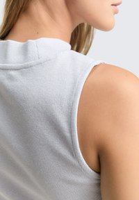 Witte geribde mouwloze top met een hoge halslijn en rauwe zoomdetails, die een zachte textuur en een getailleerd ontwerp toont.