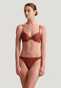 Soutien-gorge et thong assorti marron, avec des bonnets lisses agrémentés de dentelle et une taille à motif. Les bretelles réglables améliorent l'ajustement.