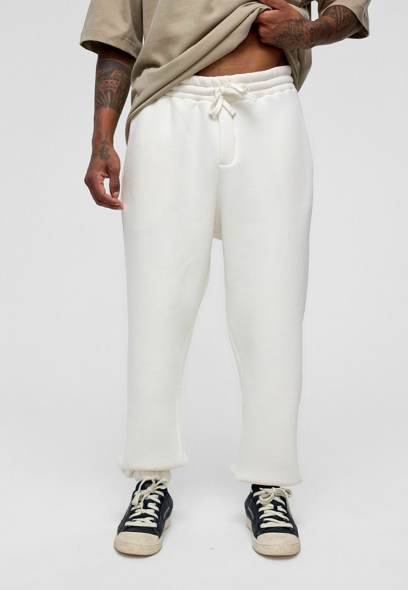 Witte, loszittende sweatpants met een trekkoord in de taille en manchetboorden, gemaakt van zacht materiaal, gecombineerd met zwarte sneakers.