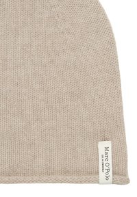 Beige gebreide muts met een getextureerd patroon. Heeft een klein wit label aan de onderrand met daarop "Marc O'Polo" gedrukt.