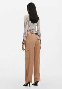 Maglietta a maniche lunghe, aderente, con stampa floreale e dettagli arricciati. Pantaloni cargo beige, larghi, con tasche laterali e una texture liscia. Scarpe nere con tacco.