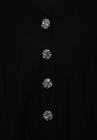 Cardigan negru cu un design în formă de v și patru butoane decorative argintii cu modele complicate. Textura pare netedă și tricotată.