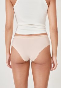 Brief in cotone rosa chiaro a coste con pizzo lungo la vita e le aperture delle gambe, abbinato a un top aderente bianco.