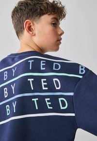 Marineblauer Pullover mit dem Schriftzug "BY TED" in weißen und hellblauen Streifen auf dem Rücken. Aus Baumwollmaterial, mit Rundhalsausschnitt und kurzen Ärmeln.