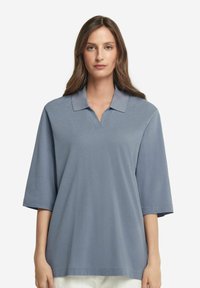 Ljusblå polo med v-ringning, kort ärm och mjuk textur, med ett subtilt mönster och en klassisk kragsdesign.