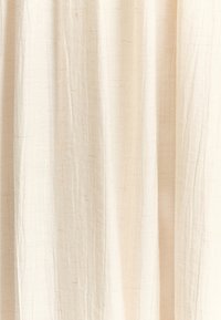 Tejido ligero y texturizado en un color beige cremoso con pliegues sutiles y hilos que se muestran de manera prominente en toda su superficie. Ideal para caer en pliegues.