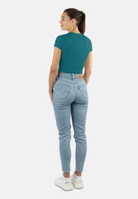 Türkises, kurzärmeliges Cropped-Top kombiniert mit hoch taillierten, hellblauen Jeans, die ein Rückentaschen-Design aufweisen, und weißen Sneakers. Schlichte und figurbetonte Stil.
