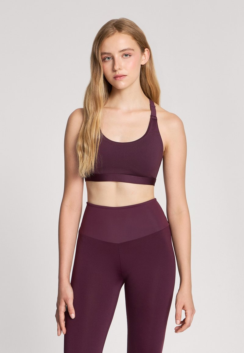 Bra sportivo bordeaux e leggings a vita alta abbinati, realizzati in tessuto elasticizzato. Il reggiseno presenta un collo a barca e spalline regolabili.