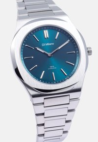 Sølv rustfrit stål ur med en teal urskive, minimalistiske time markeringer og datovisning, der har en børstet overflade og integreret bracelet design.