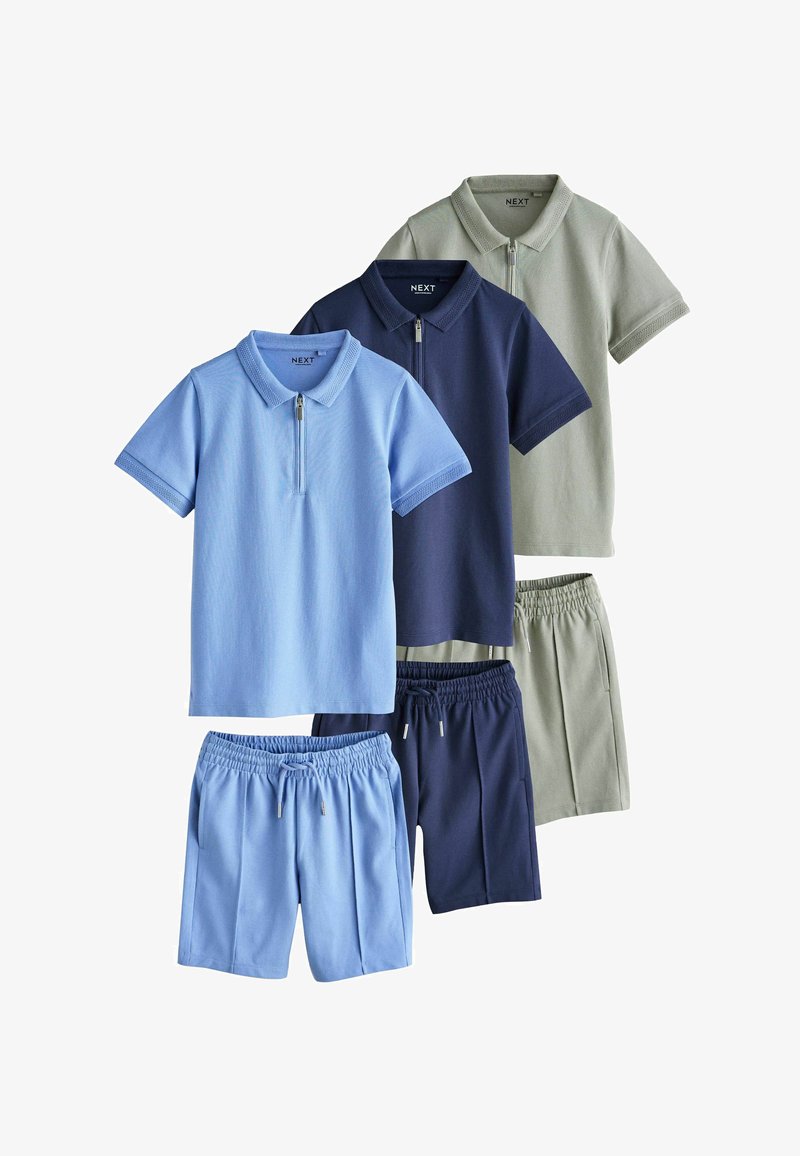 Trois ensembles de polos à manches courtes avec fermeture éclair et shorts à taille élastique en bleu clair, bleu marine et gris clair, disposés sur fond blanc.