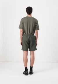 T-shirt à manches courtes vert olive et shorts assortis. Les shorts sont dotés d'une taille élastique, d'une poche latérale et d'une coupe décontractée. Chaussures noires.
