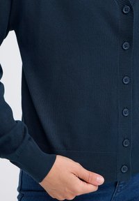 Cardigan lavorato a maglia blu navy con scollo a V, maniche lunghe e sei bottoni. Dettagli a coste sui polsini e sull'orlo. Texture morbida.