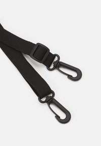 Correia de nylon preta com fivela ajustável e dois clips metálicos pretos em cada extremidade para fixação. Textura plana e design robusto.