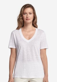 Vit V-ringad T-shirt i lätt, texturerat tyg. Korta ärmar och avslappnad passform, med synlig sömnad längs halsringningen.