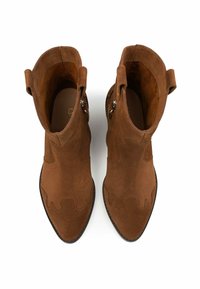 Stivaletti alla caviglia in suede marrone con punta affusolata e dettagli cuciti a onde, dotati di cerniera e linguette per una facile vestibilità. Suola piatta.
