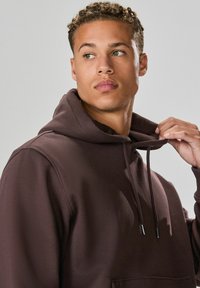 Brauner Kapuzensweatshirt aus weichem Material, ausgestattet mit einer Kängurutasche, verstellbaren Kordeln und einer lässigen Passform.