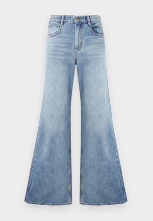 Vartalonmyötäiset siniset farkut, joissa on leveä lahje ja vaalea pesu. Etutaskut ovat tikattuja ja niissä on kiillotetut metalliset napit.