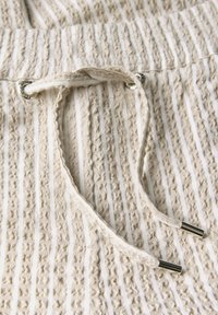 Light beige shorts with textured vertical stripes, featuring a drawstring with metallic aglets and eyelets for adjustment.