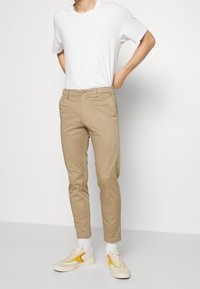 Beige bomullschinos med slim fit, med knappstängning och sidofickor, kombinerat med en slät vit t-shirt och vita sneakers.
