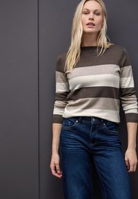 Brązowy i beżowy sweter w paski z rękawami 3/4, zestawiony z ciemnoniebieskimi dżinsami. Prosty wzór, miękka tekstura i klasyczny krój.