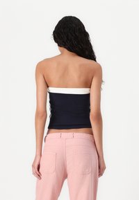 Navy and white strapless top with a fitted design, paired with light pink loose-fitting pants featuring back pockets and a textured fabric.