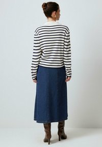 Randig långärmad tröja i cream och marinblå, kombinerad med en blå denimkjol och bruna klackstövlar. Bakifrån framhävs former och texturer.