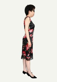 Robe florale noire avec des fleurs rouges, corsage ajusté et jupe longueur genoux. Texture satin lisse et léger éclat, associée à des talons noirs.