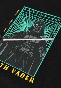 Musta t-paita, jossa on grafiikka hahmosta, joka heiluttaa valosarjaa, ympäröitynä teal-värisestä geometrisesta ruudukosta, ja keltaisella tekstillä "Darth Vader."