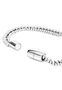 Hopeaketti hopeasta, jossa on helmimallinen muotoilu; varustettu sylinterimäisellä lukolla, jossa on kaiverrettu brändäys. Liukas, heijastava pinta.