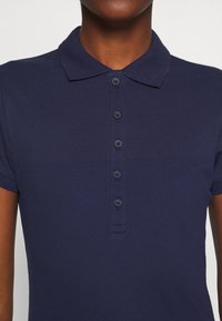 Polo-shirt bleu marine foncé avec une texture douce, doté d'un col classique et d'une patte de boutonnage à six boutons, vu de la poitrine vers le haut.