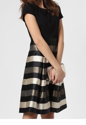 Černý top s rozšířenou sukní se širokými horizontálními pruhy v zlaté a krémové barvě. Textura je hladká s kovovými akcenty. Malé kovové psaníčko.