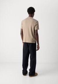 T-shirt beige in cotone con maniche corte e taglio dritto, abbinato a jeans larghi blu scuri e calzature marroni.