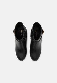 Para czarnych skórzanych botków za kostkę z bocznymi zamkami i złotymi klamrami, widziana z góry na białym tle.