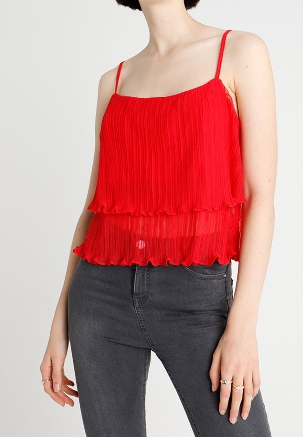Haut sans manches plissé rouge avec un design à volants superposés, doté de fines bretelles et d'une texture transparente, associé à un jean gris ajusté.
