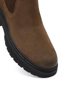 Stivale alla caviglia in suede marrone con punta rotonda, pannelli elastici laterali e suola in gomma nera spessa con battistrada pronunciato per garantire aderenza.