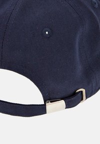 Gorra de béisbol azul marino con textura de tela, que cuenta con una hebilla de metal plateado en la parte posterior para ajuste y ojales de ventilación en la corona.