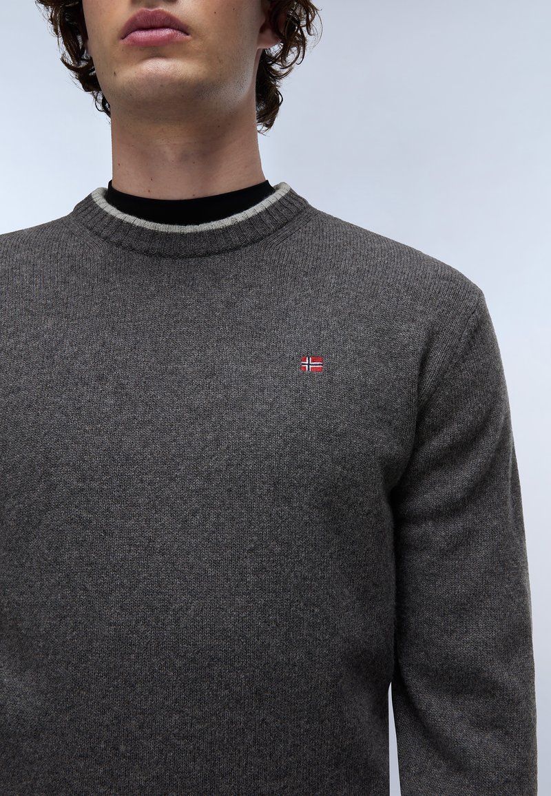 Szary sweter z dzianiny z prążkowanym okrągłym dekoltem, z małą haftowaną norweską flagą na piersi oraz teksturowanym materiałem.