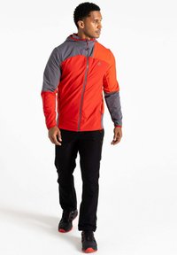 Rote und graue Kapuzenjacke mit Reißverschluss, die ein geometrisches Design aufweist. Kombiniert mit schwarzen Hosen und schwarzen Turnschuhen mit roten Akzenten.