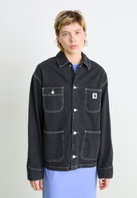 Črna denim jakna z belimi šivi, ki ima dva sprednja žepa in majhen logotip. Dolgi rokavi z gumbi.
