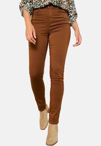 Pantaloni marroni slim fit con una texture liscia, vita alta e stile a cinque tasche, abbinati a stivaletti beige alla caviglia e una maglia fantasia.